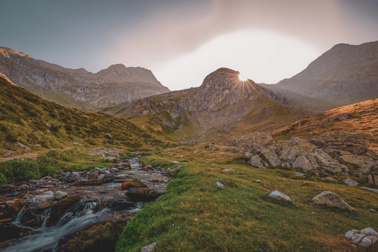 Paysage époustouflant des Pyrénées, vallée verdoyante, montagnes majestueuses et soleil couchant.