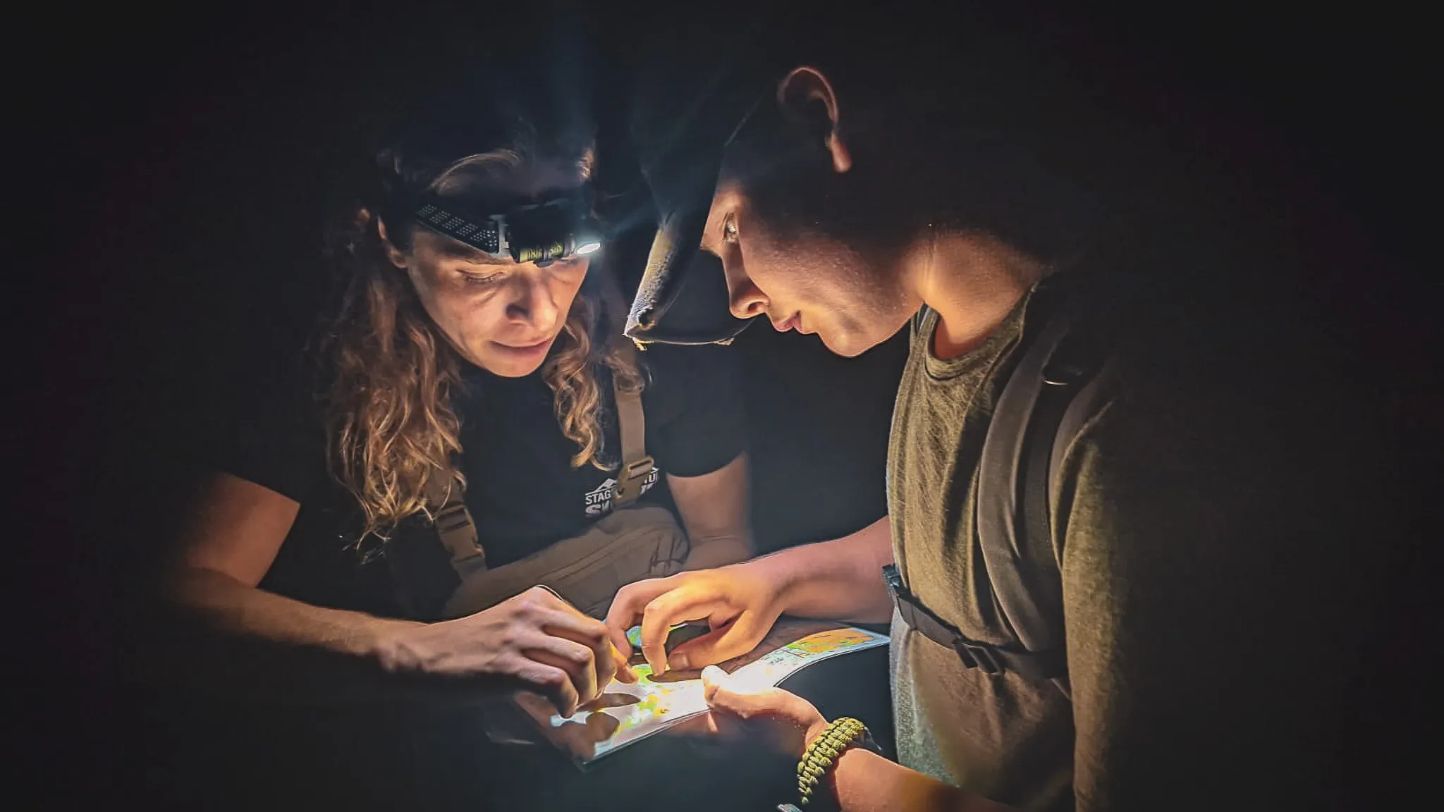 Deux personnes examinent attentivement une carte sous une lumière tamisée, en pleine nature.