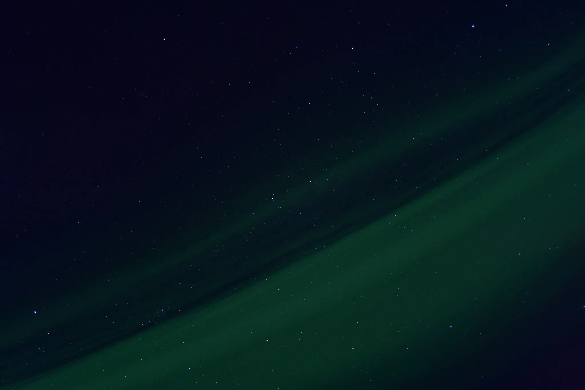 Un ciel nocturne parsemé d'étoiles scintillantes, où une aurore boréale verte se déploie horizontalement, créant un contraste avec les teintes sombres de l'espace.