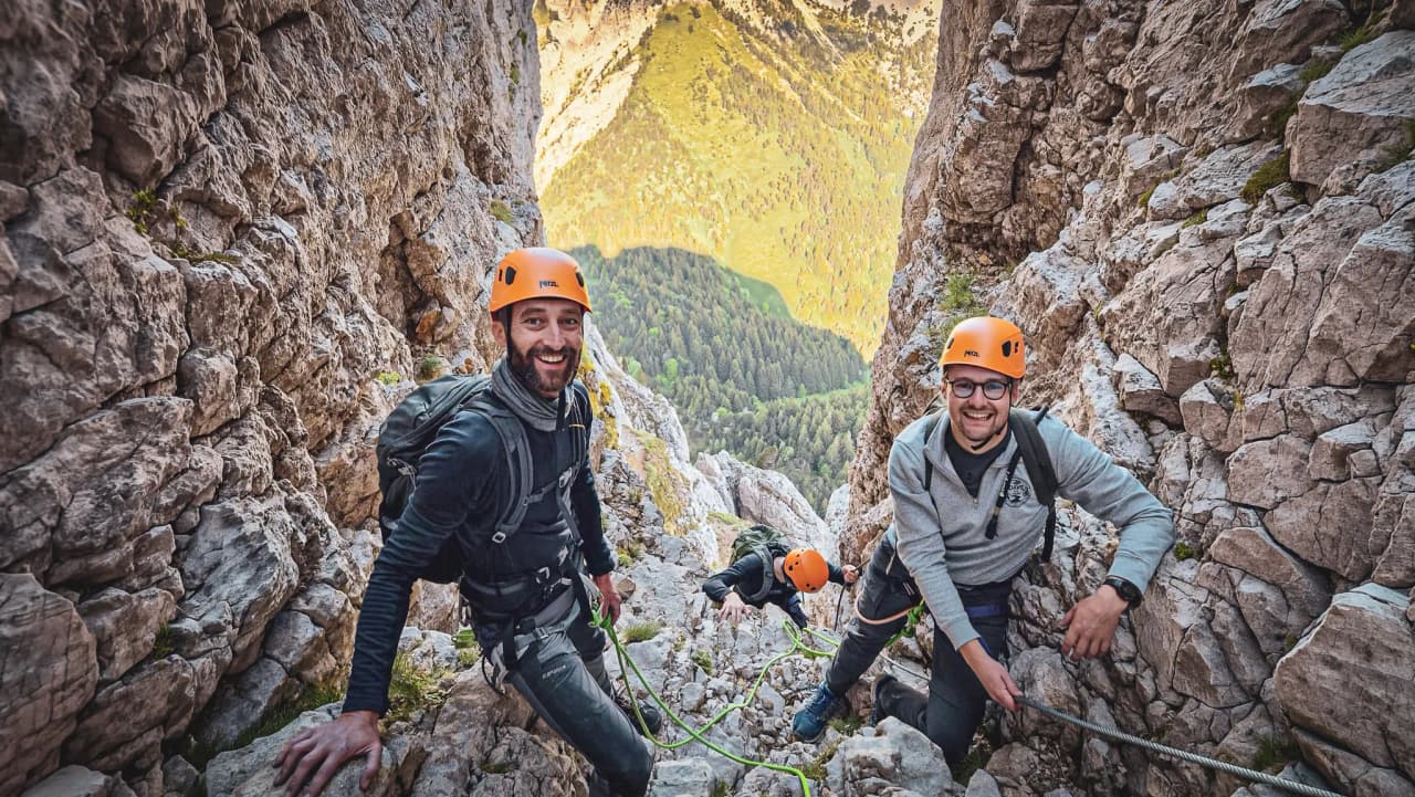 Three smiling climbers in a rock crack, surrounded by lush green countryside.