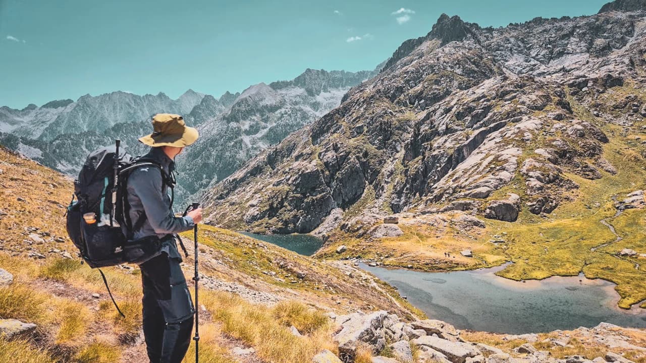 Randonneur admirant un panorama majestueux des Hautes Pyrénées, entre lacs et montagnes.