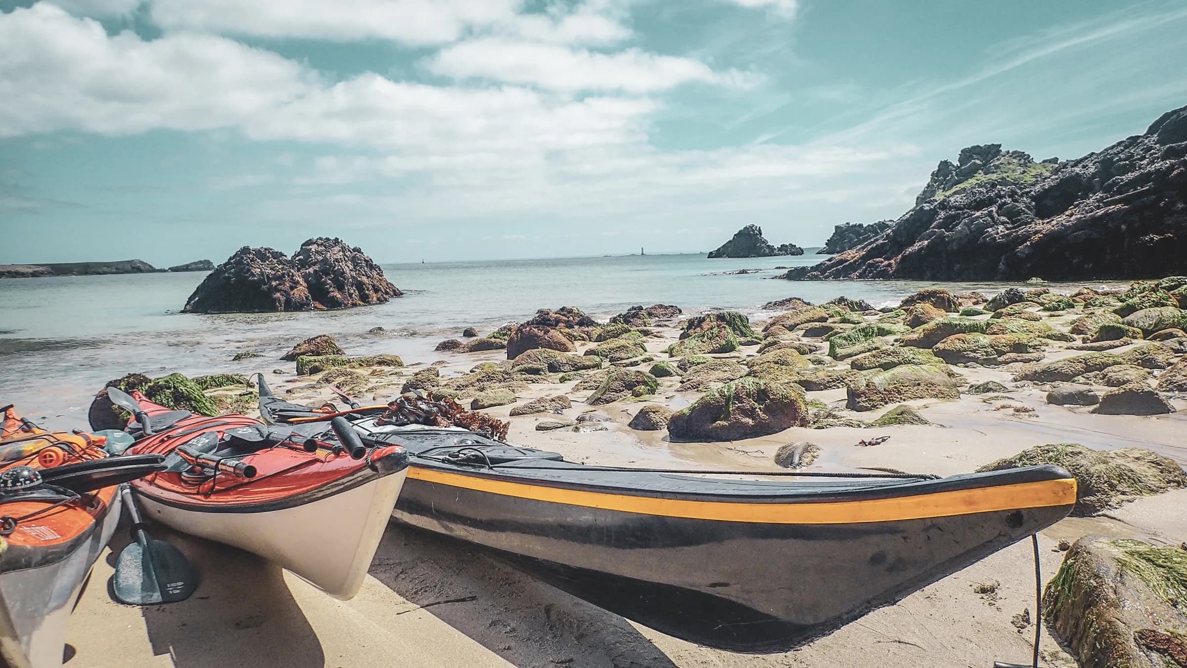 Colourful canoes on a beach in the Molène archipelago, between rocks and sparkling sea.