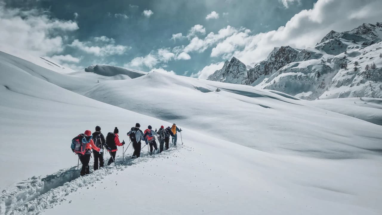 Group of hikers on snowshoes in a snow-covered alpine landscape, with mountains in the background.