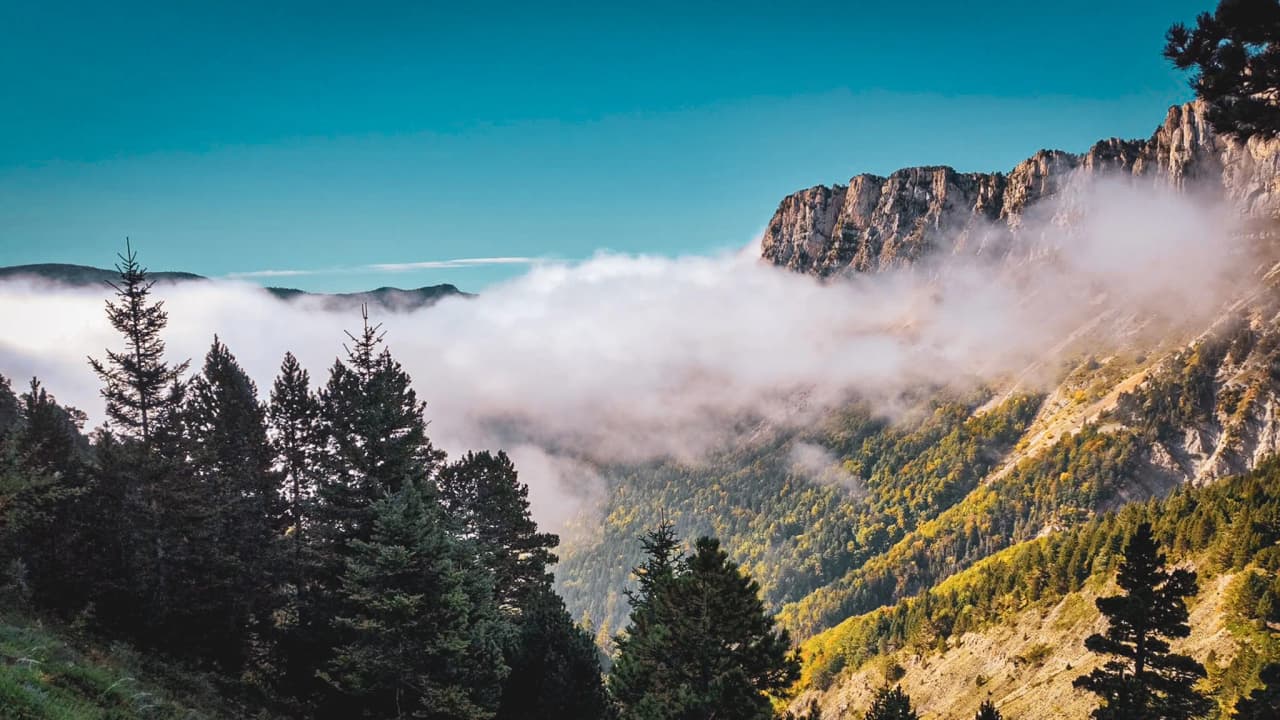 Spectacular panorama of Mont Aiguille, with clouds flirting with the peaks and lush forest.
