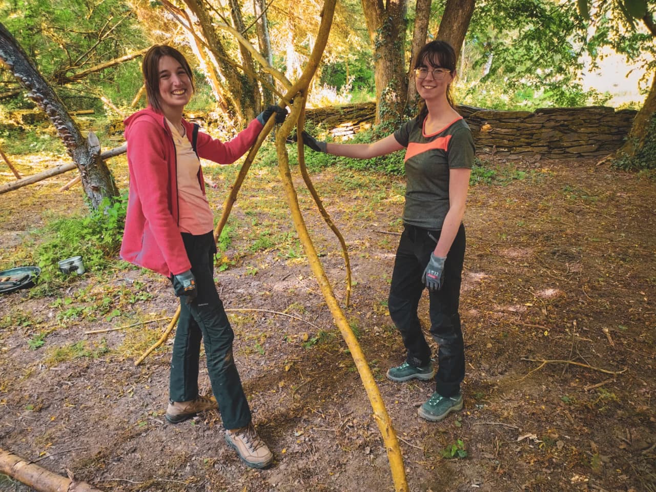 Deux jeunes femmes souriantes en pleine activité de survie en forêt, entourées de verdure.