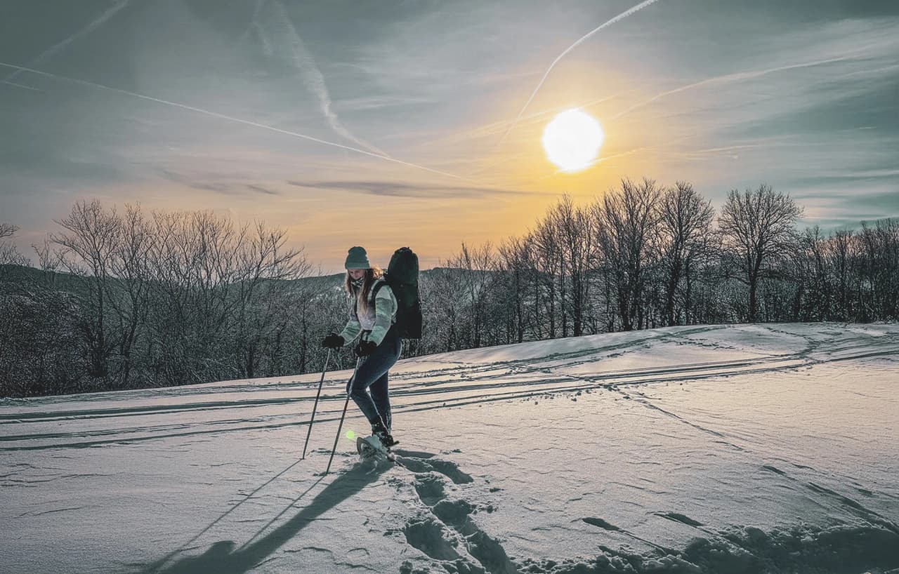 Woman on snowshoes on a Vosges ridge, silhouetted against an enchanting sunset.