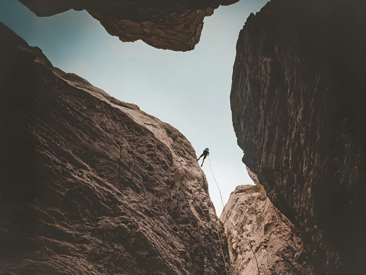 A climber pulls himself up a majestic rock face under clear skies, offering an impressive view.