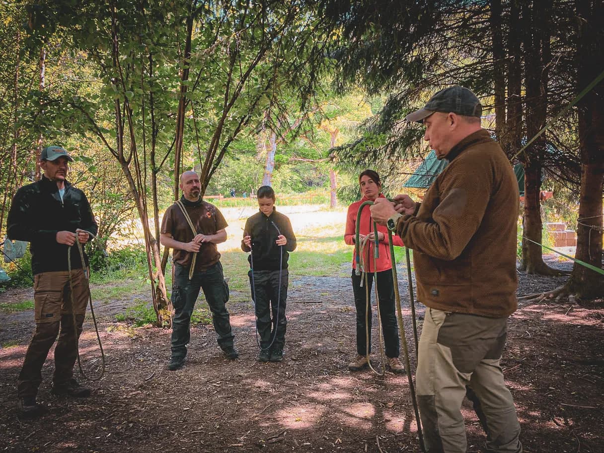 Groupe en pleine nature apprenant des techniques de survie en forêt, entouré d'arbres verdoyants.