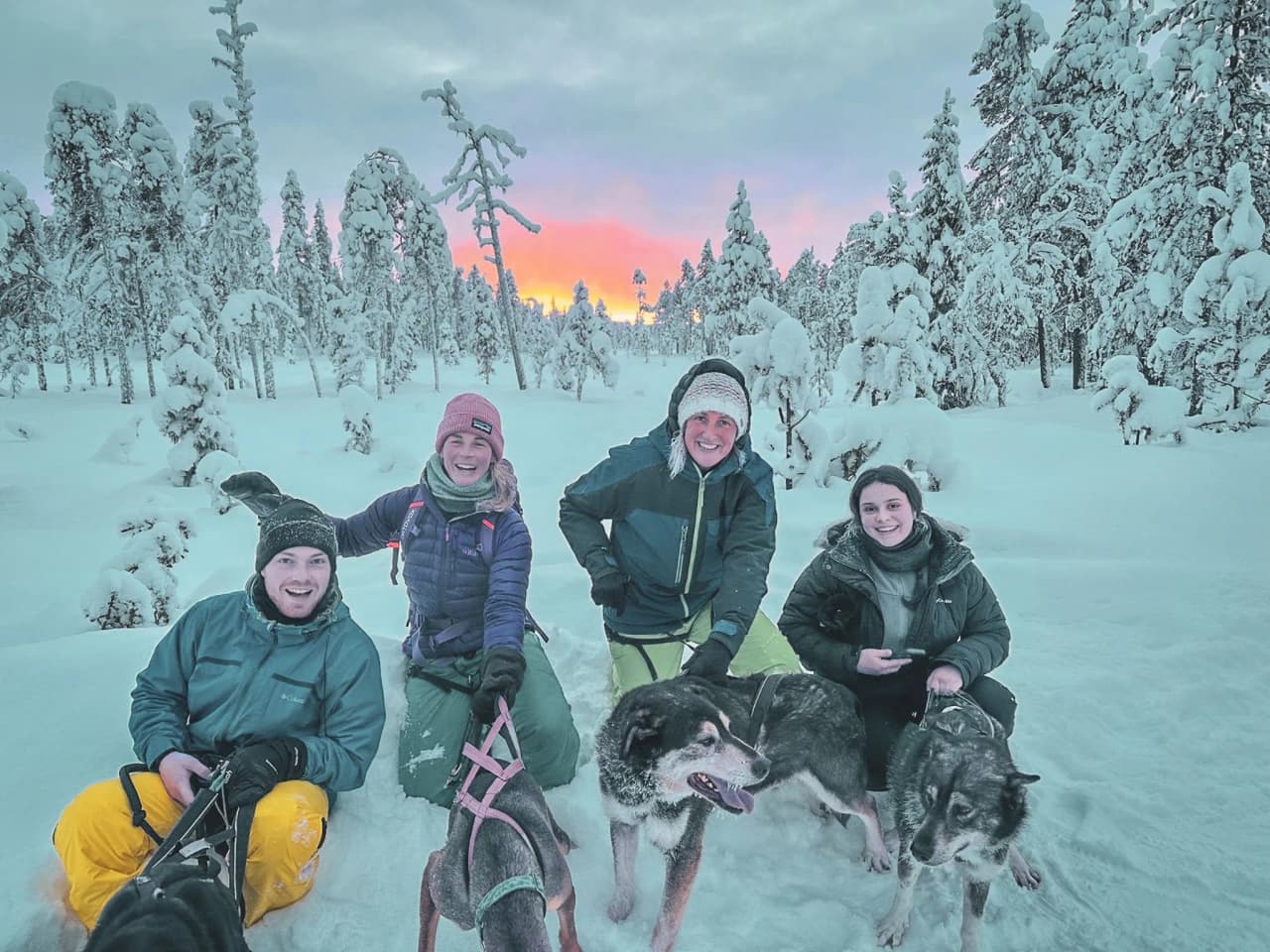 A smiling group with sled dogs in a magical winter landscape in Lapland.
