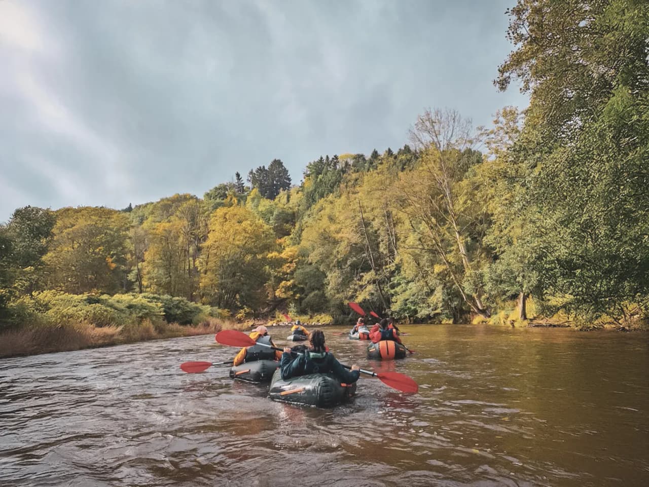 Groupe de randonneurs en packraft naviguant dans une rivière entourée de forêts colorées en Ardenne.