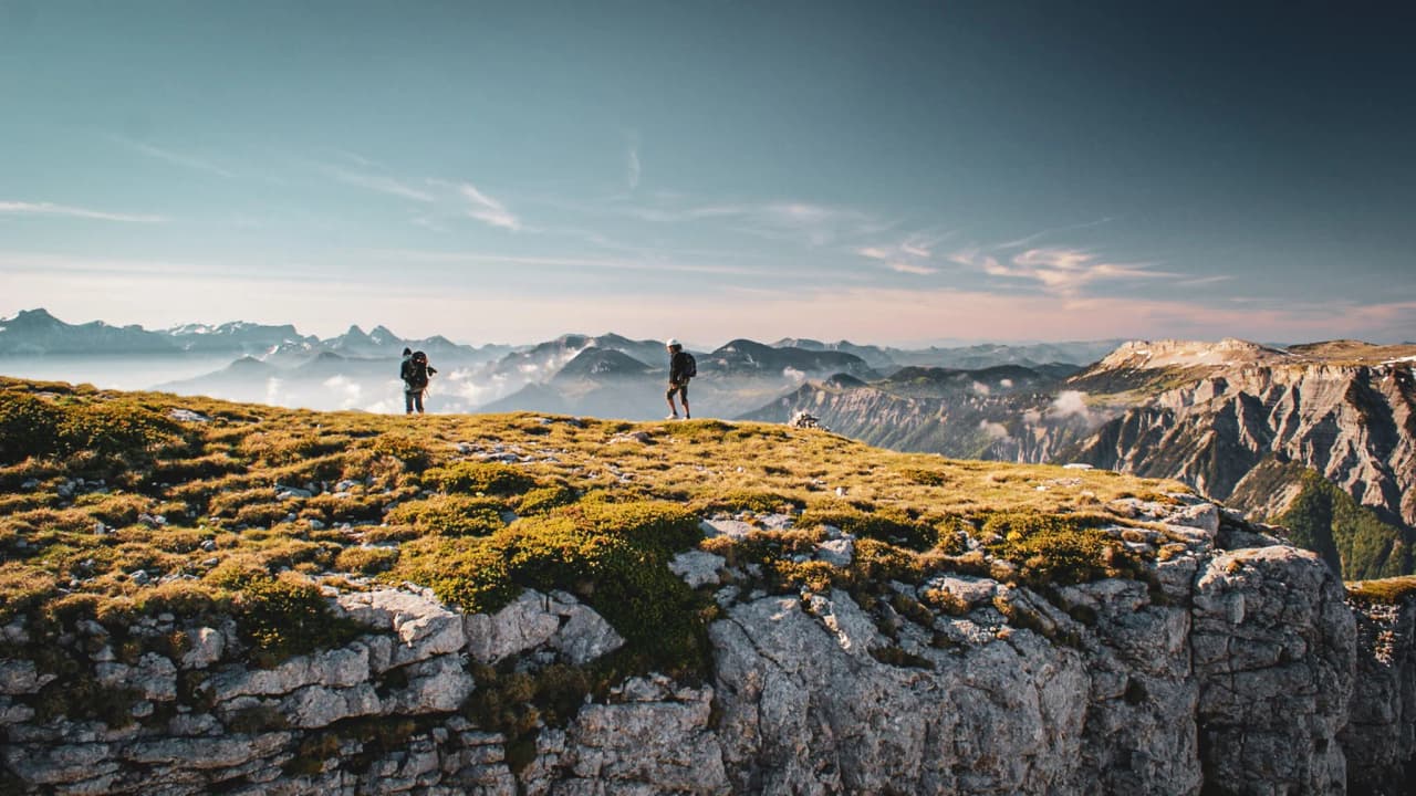 Hikers on a verdant summit, admiring a spectacular panorama of the surrounding mountains.