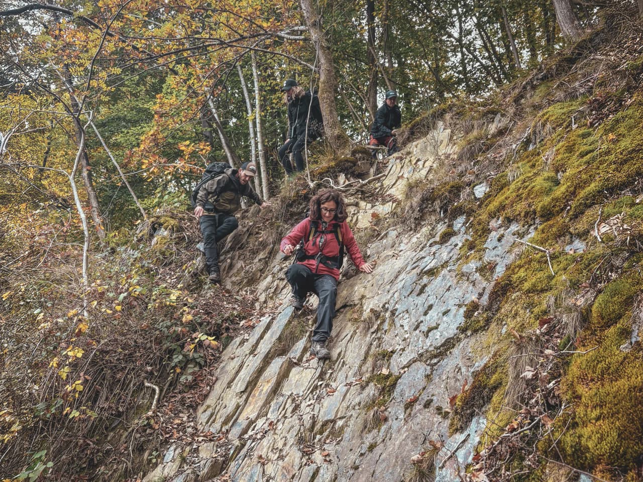 Un groupe d'aventuriers descend un sentier escarpé en forêt, entouré de couleurs automnales.
