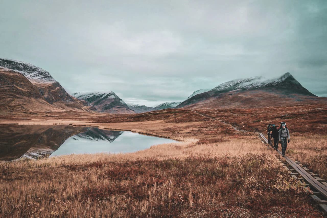 Randonneurs sur un sentier en bois, entourés de montagnes et d'un lac paisible en Laponie.
