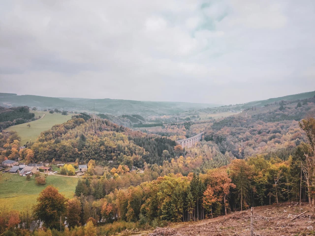 Paysage automnal des Ardennes, vallées verdoyantes, pont majestueux et forêts colorées.