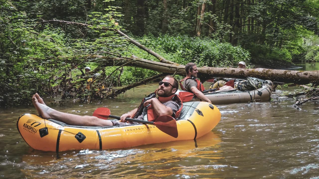 Des pagayeurs relaxent en packraft sur une rivière verdoyante, entourés de nature.