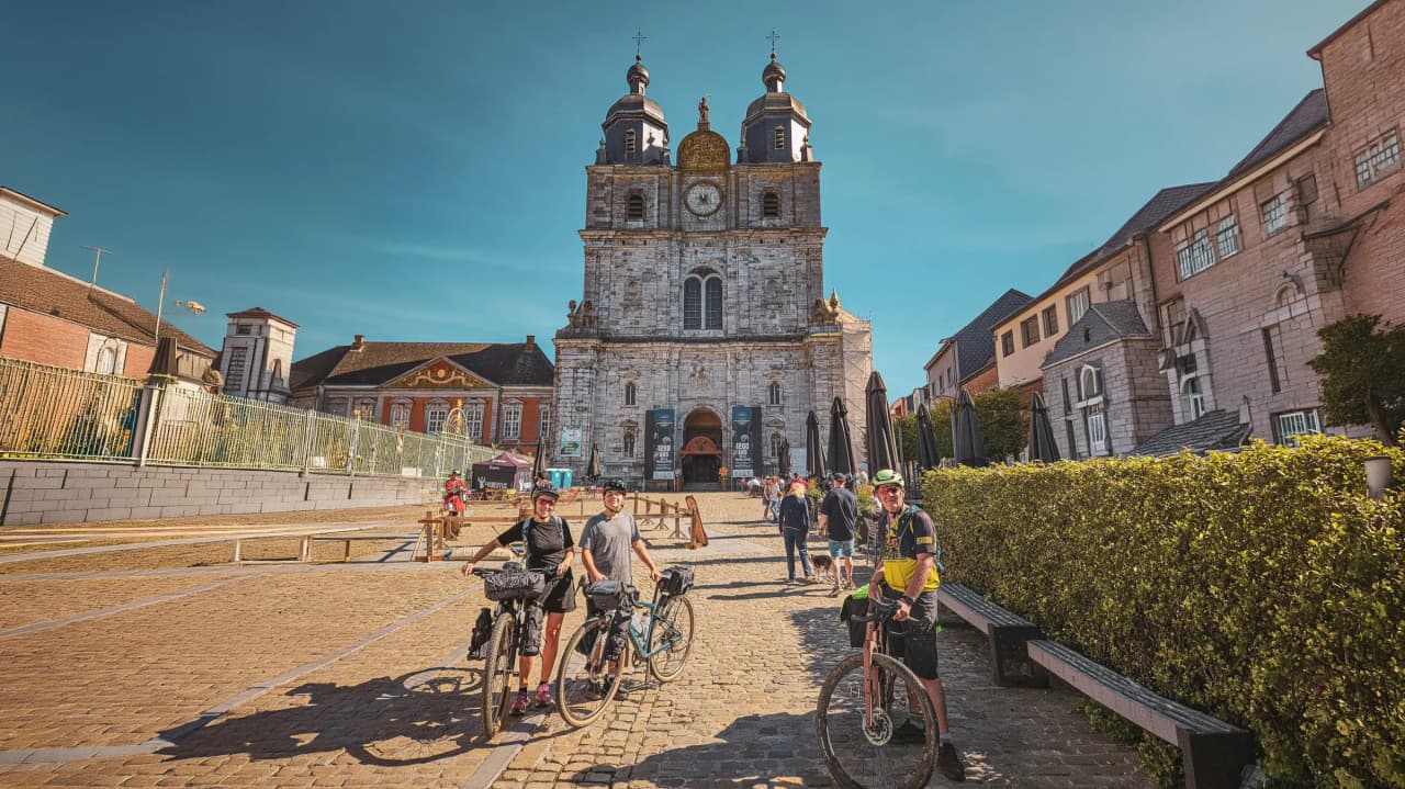 Three cyclists in front of a beautiful church, ready for an adventure in the Ardennes forests.