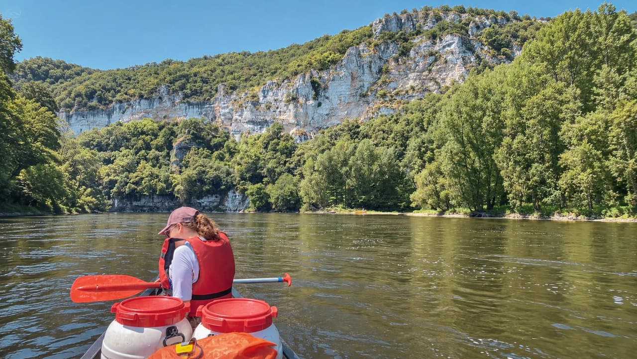 Canoë sur la Dordogne, entouré de falaises verdoyantes et d'une nature luxuriante.