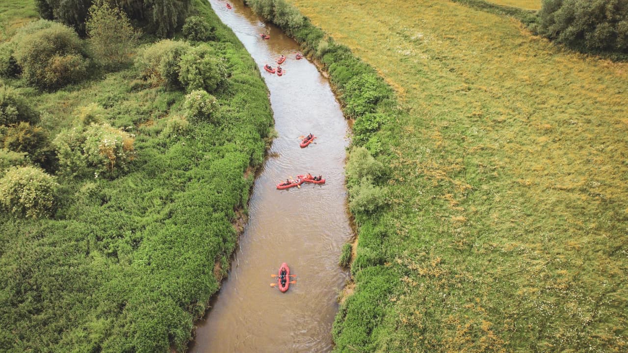 Une paisible rivière serpente entre la verdure, des packrafts rouges glissent sur l'eau, invitant à l'aventure.