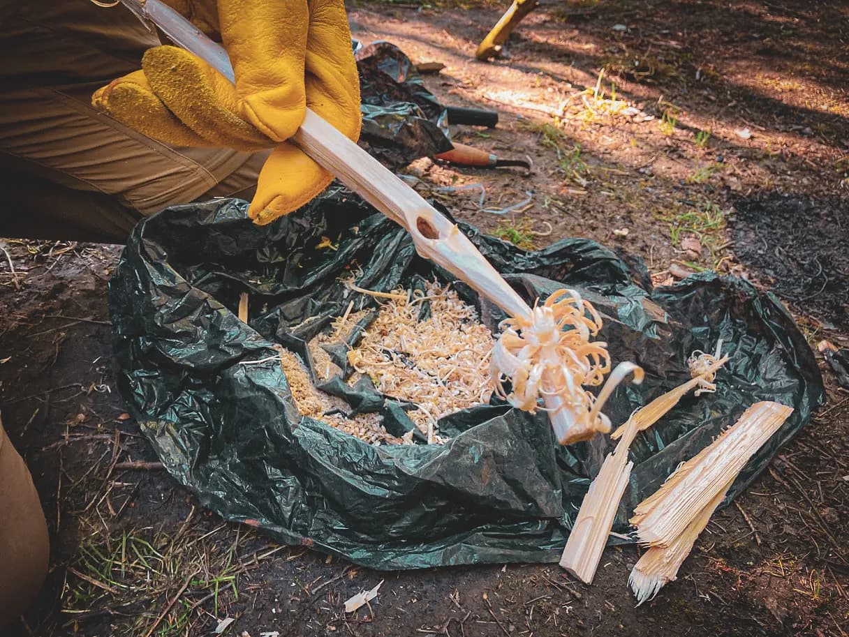 Un participant en stage de survie façonne du bois dans la forêt, découvrant l'art de la survie.