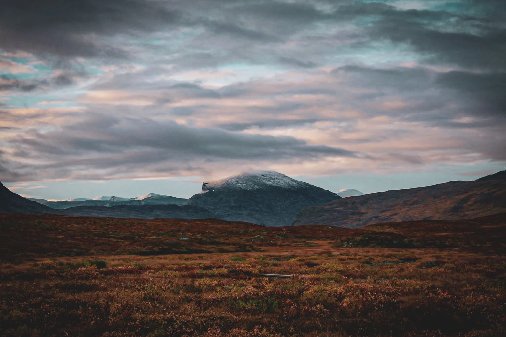 Un paysage montagneux avec des montagnes majestueuses en arrière-plan, certaines recouvertes de neige. Le ciel est partiellement nuageux, avec des nuances de bleu et des teintes pastel. Au premier plan, une vaste plaine.