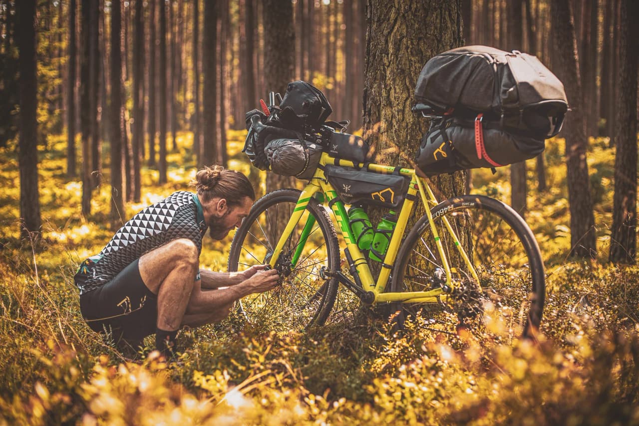 Cyclist in the countryside, repairing his bike in the heart of the Ardennes forests, golden light.