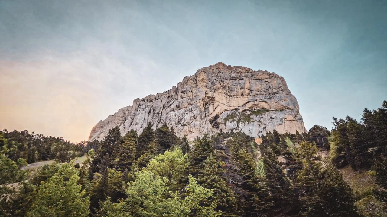 The majestic Mont Aiguille, surrounded by lush green forests beneath a clear blue sky. An adventure guaranteed!