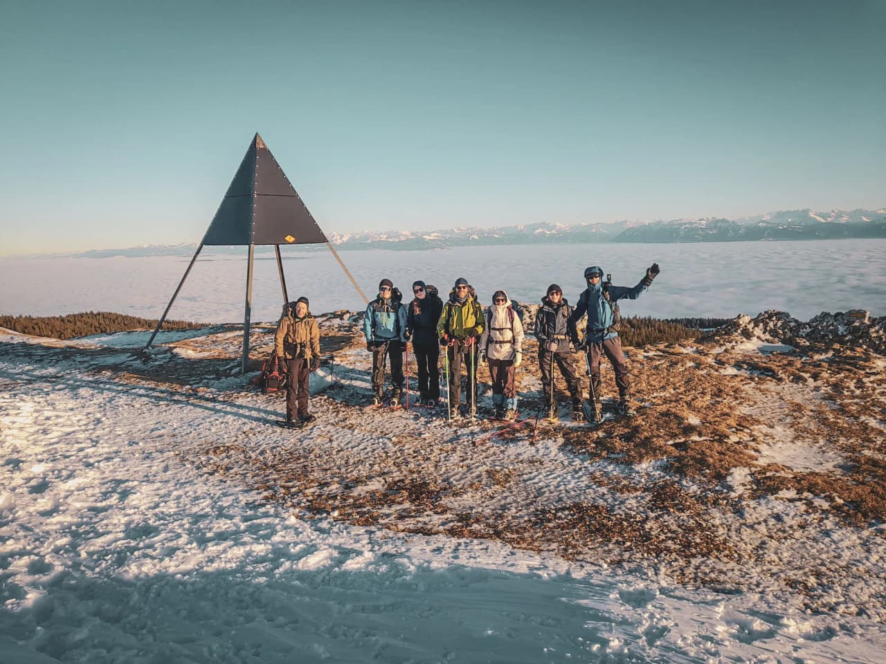 A group of adventurers on snowshoes on a snow-covered summit, with a spectacular panorama of the Swiss Jura.