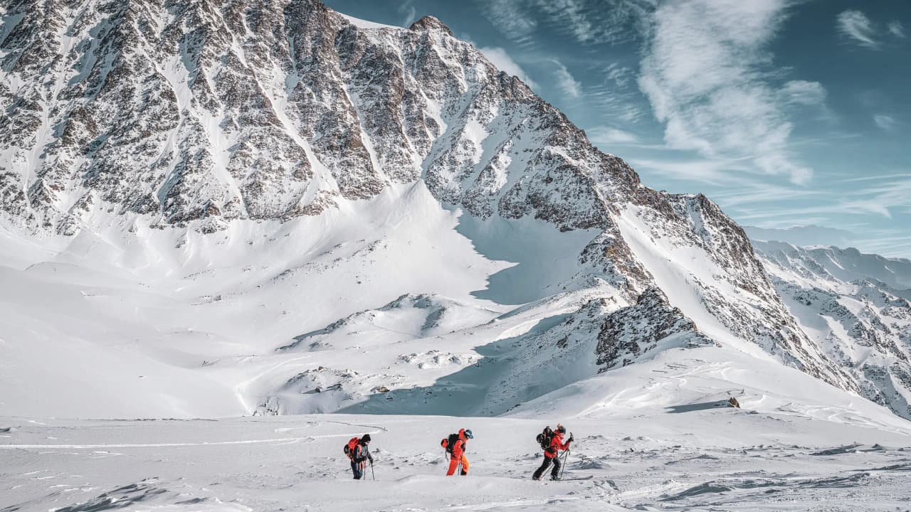 Three hikers make their way across the immaculate snow, surrounded by majestic peaks.