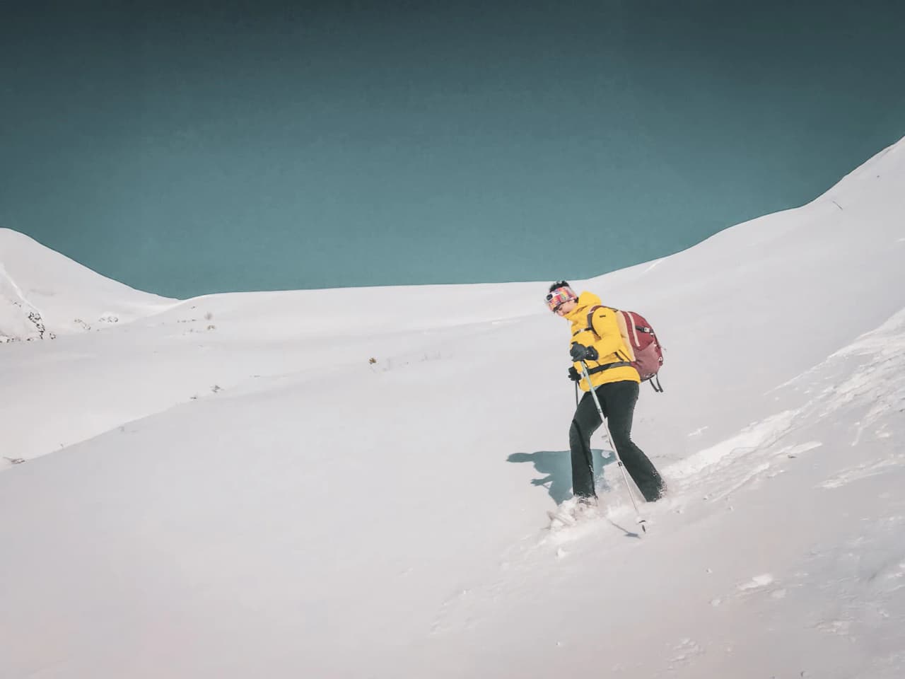 A snowshoe hiker, dressed in yellow, explores a snow-covered landscape facing majestic glaciers.