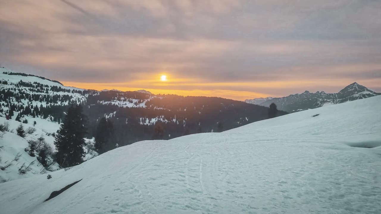 A dazzling sunset over snow-capped mountains, inviting you to embark on a ski touring adventure.