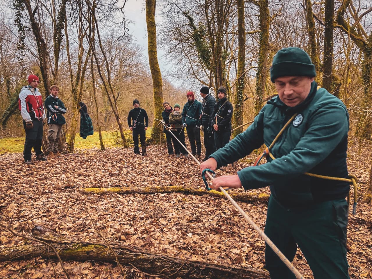 Groupe en forêt lors d'un stage de survie, apprenant à tisser des cordes pour l'aventure.