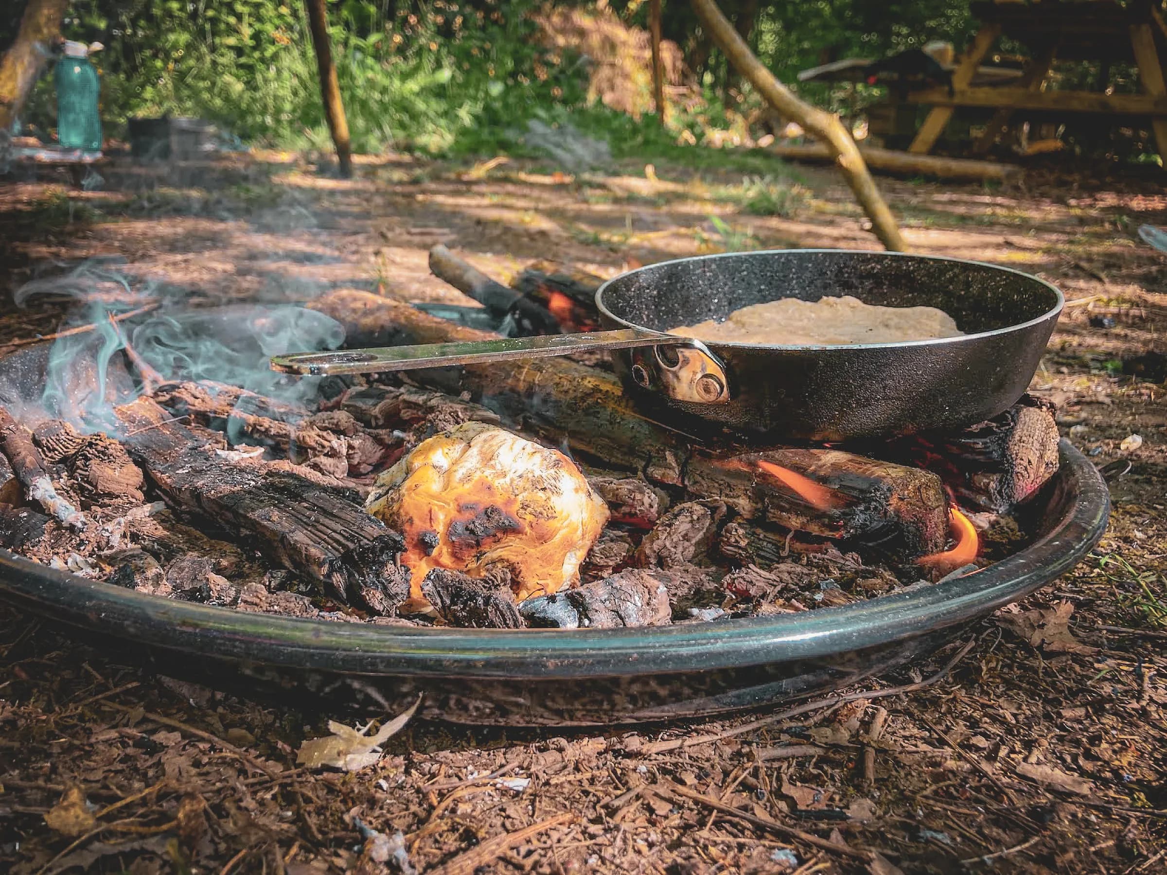 Un feu de camp crépitant avec des morceaux de bois et une poêle cuisinant en pleine nature.