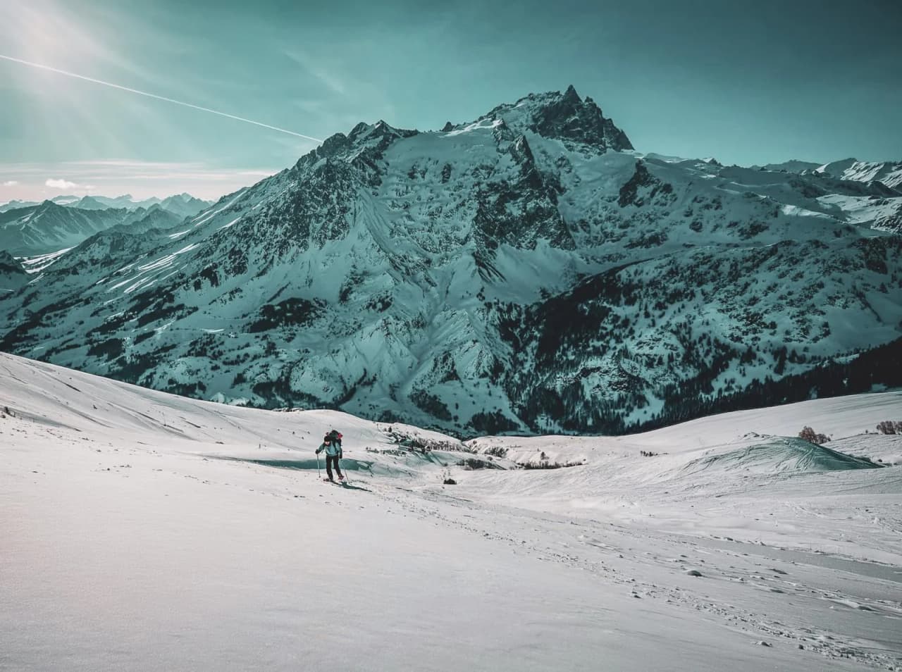 A person on snowshoes crosses a snow-covered landscape with the majestic Meije in the background.