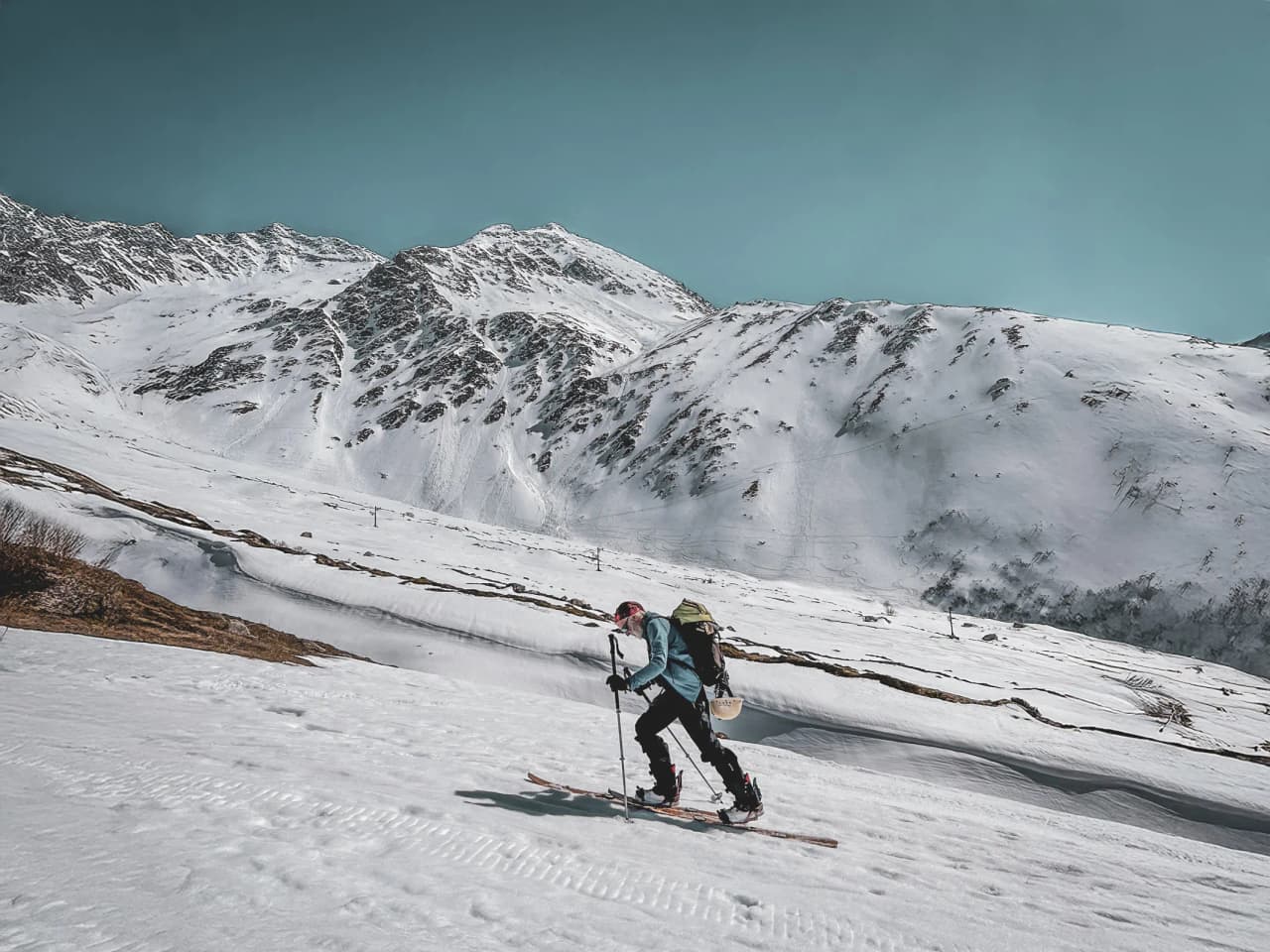 Man on ski touring across a vast snow-covered alpine landscape, majestic peaks in the background.