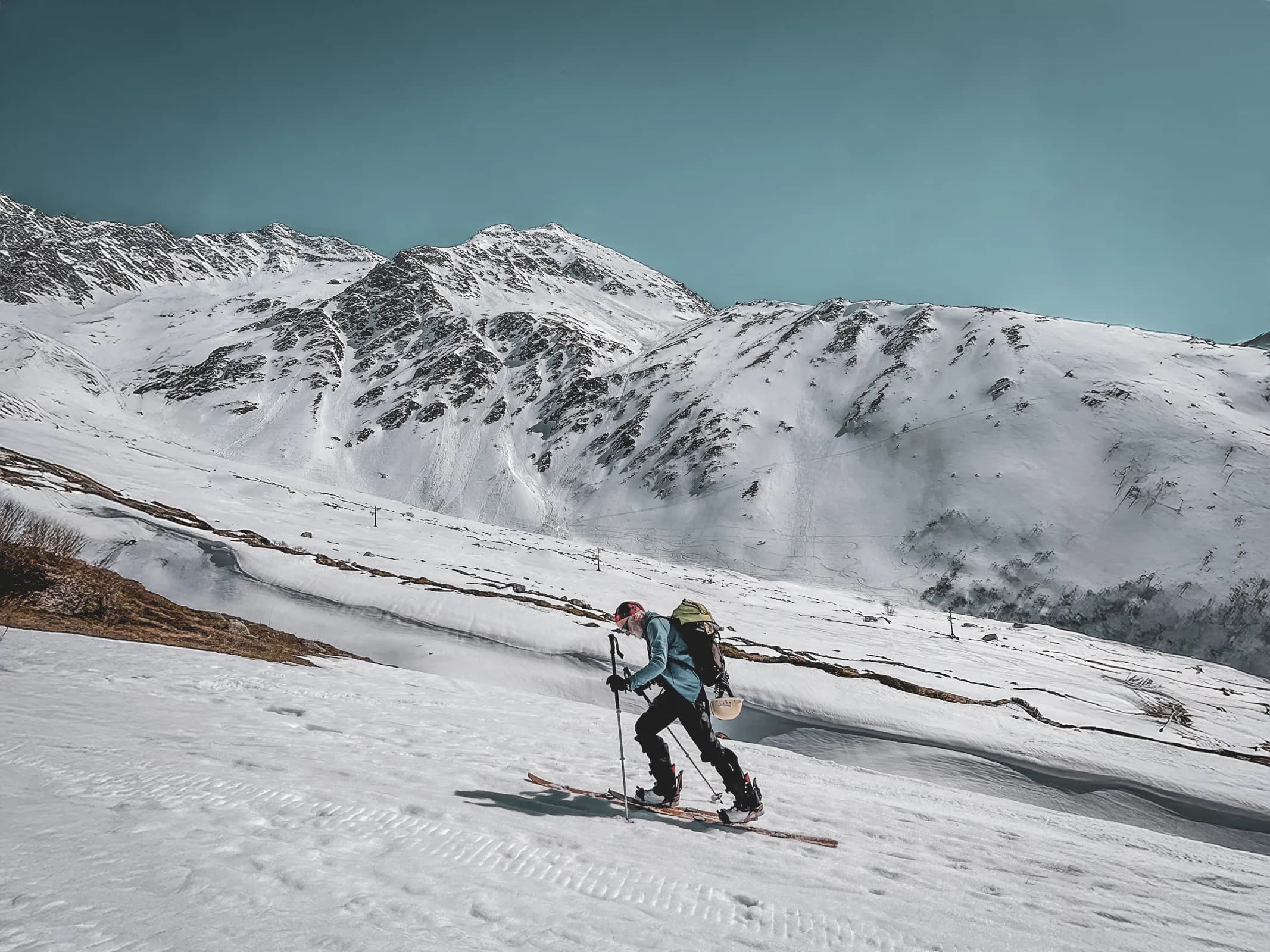 Man on ski touring across a vast snow-covered alpine landscape, majestic peaks in the background.