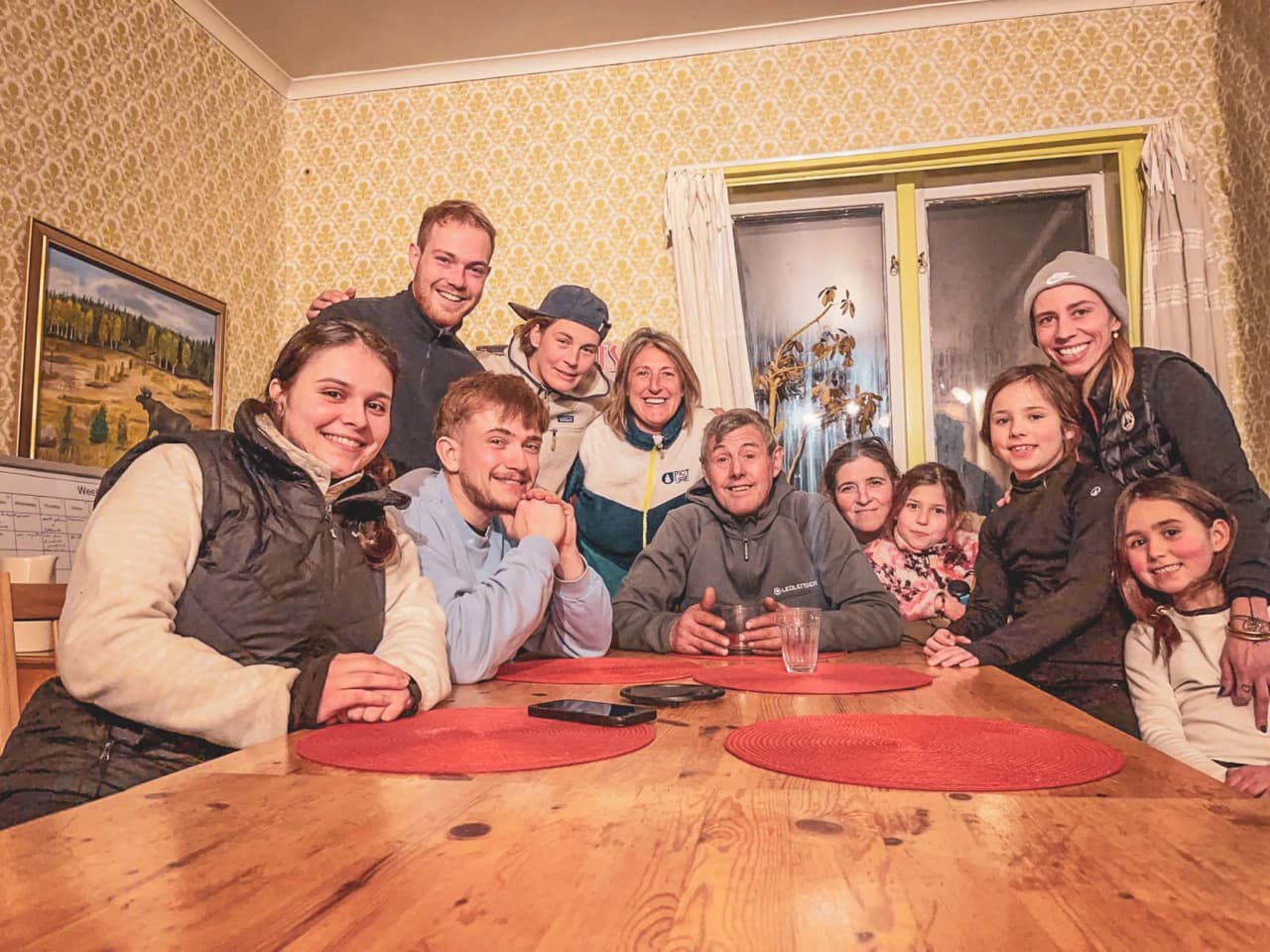 A smiling group around a wooden table in a cosy Lapland chalet, ready for adventure.