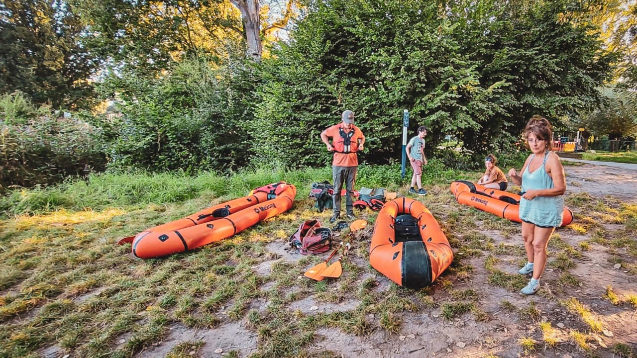 Équipe prête pour une aventure en packraft au bord d'une rivière, entourée de nature.