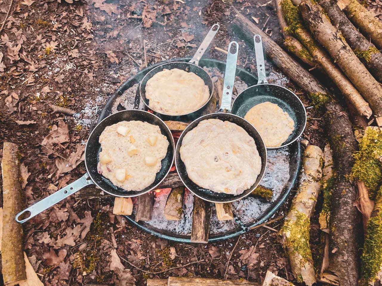 Casseroles sur un feu de camp, préparant un repas face à la nature paisible de l'Ardenne.