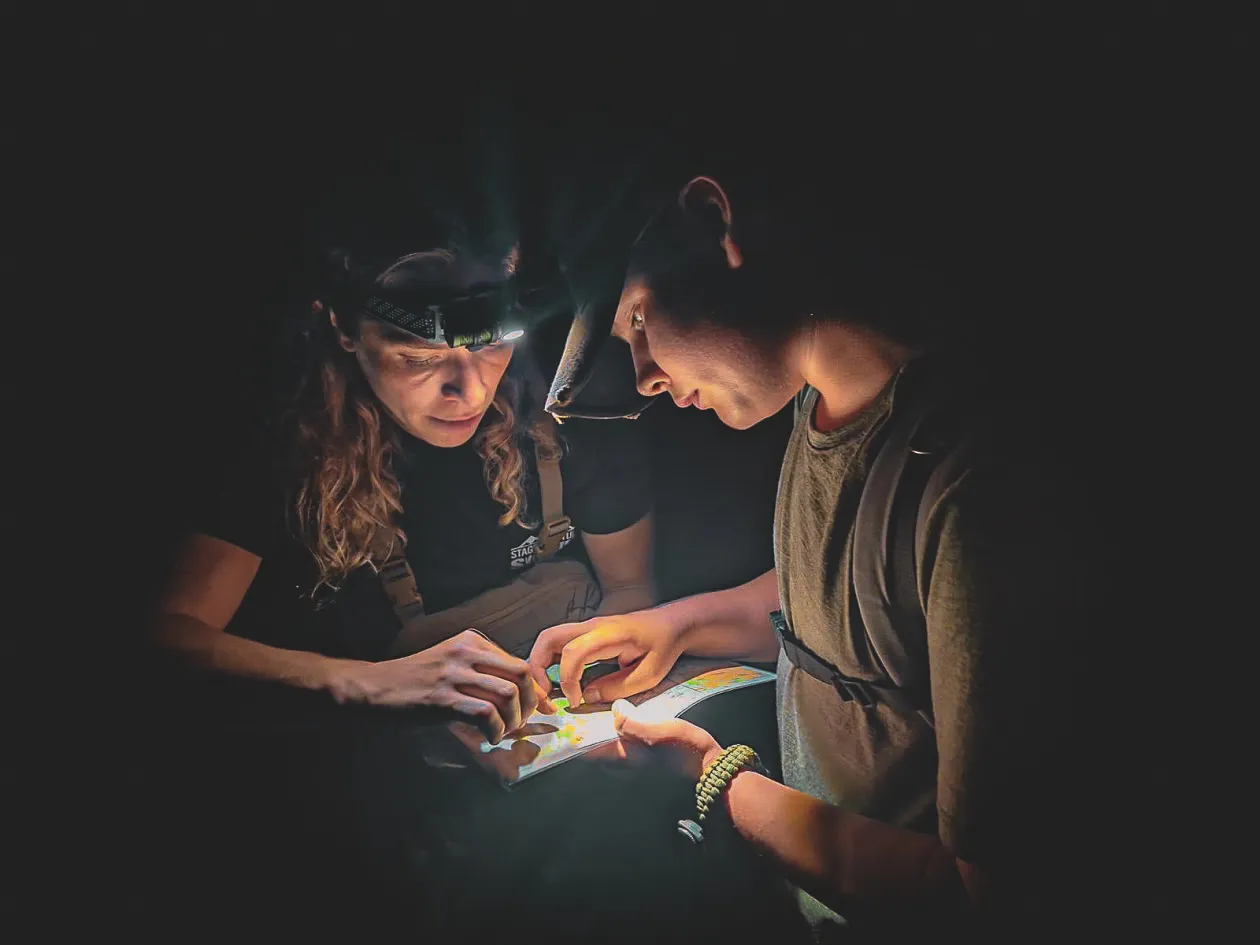 Deux personnes étudient une carte à la lumière frontale, plongées dans l'aventure nocturne.