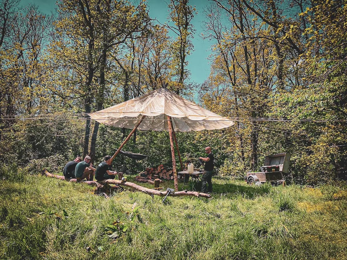 Un groupe en pleine nature, sous une toile, apprend à survivre en forêt verdoyante.