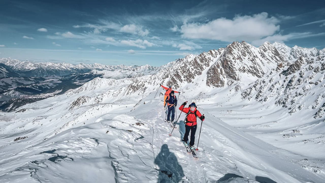 A group of skiers on an alpine hike on a snow-covered summit, with majestic mountains in the background.