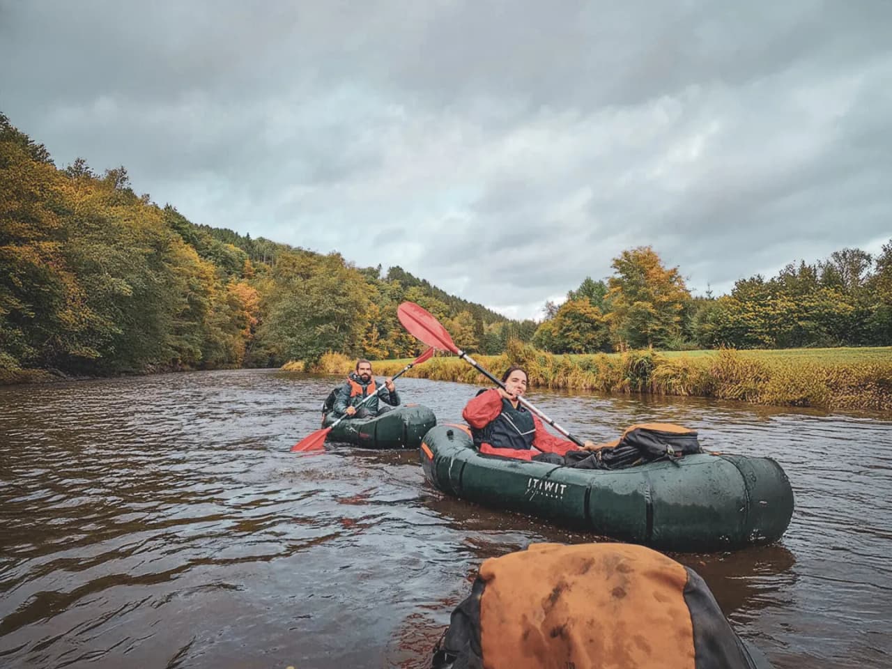 Deux aventuriers pagaient en packraft sur une rivière bordée de forêts colorées en automne.