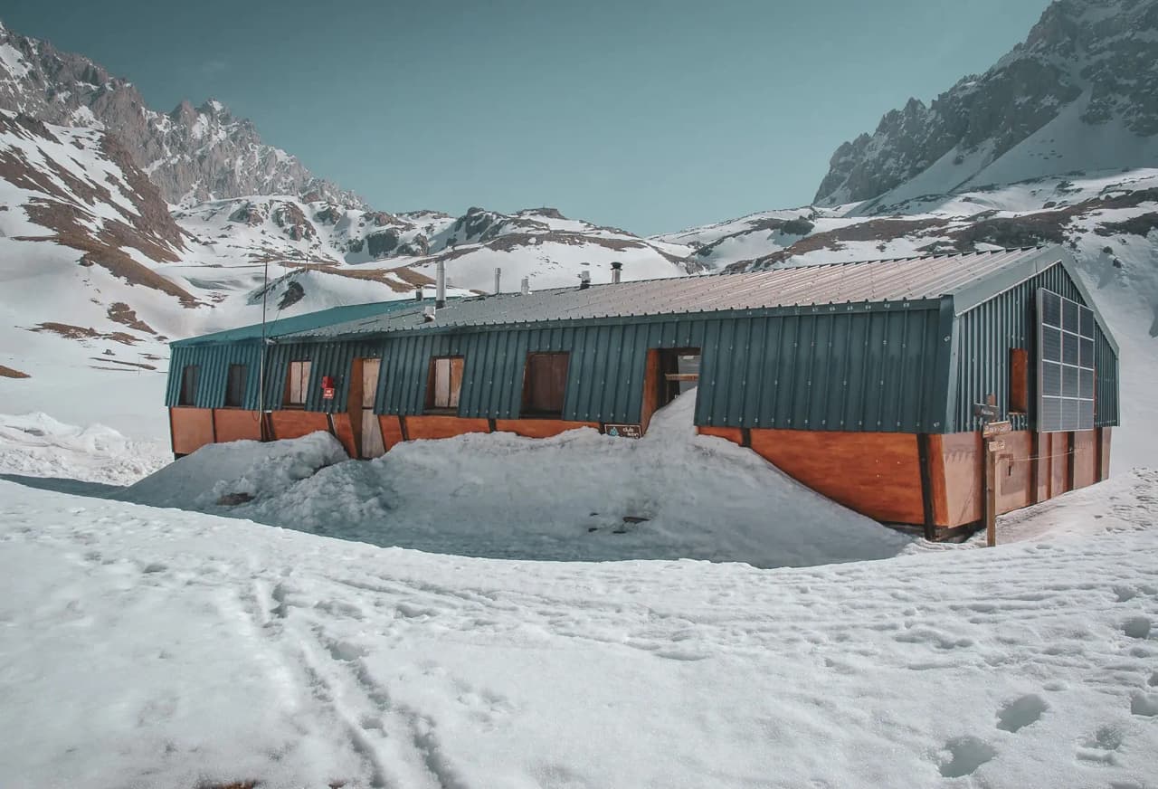 A wooden Mountain hut surrounded by snow, with majestic mountains in the background, an invitation to adventure.