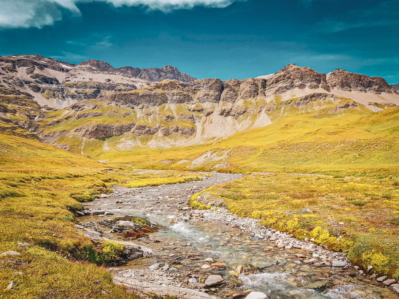 Un paysage alpin à couper le souffle, avec des montagnes majestueuses, des prairies verdoyantes et un ruisseau cristallin.