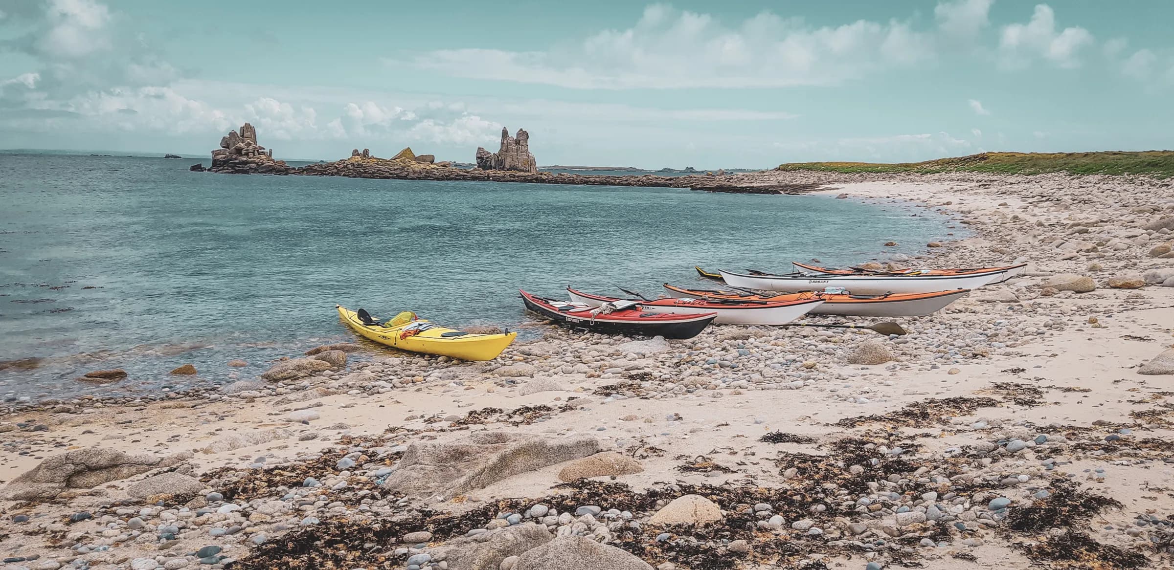 Five colourful kayaks on a tranquil beach, surrounded by azure waters and rock formations.