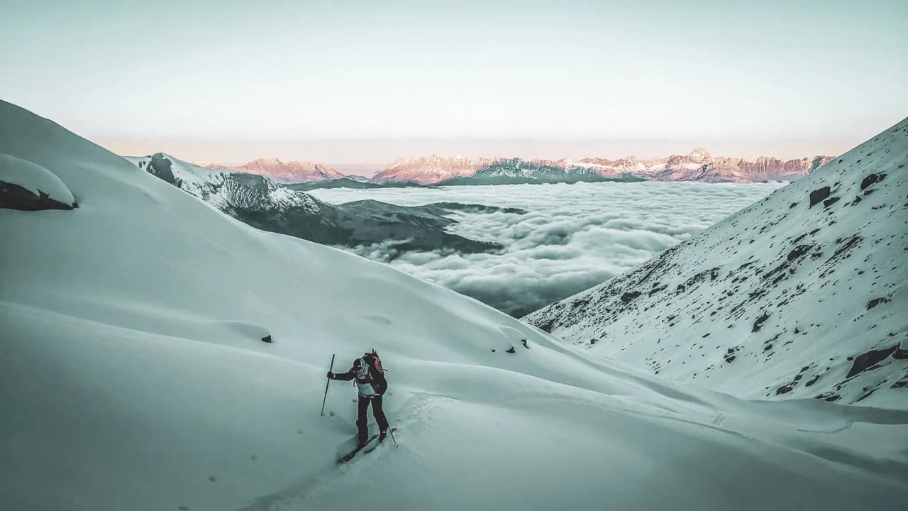 A lone skier explores a majestic snowscape with mountains in the background.