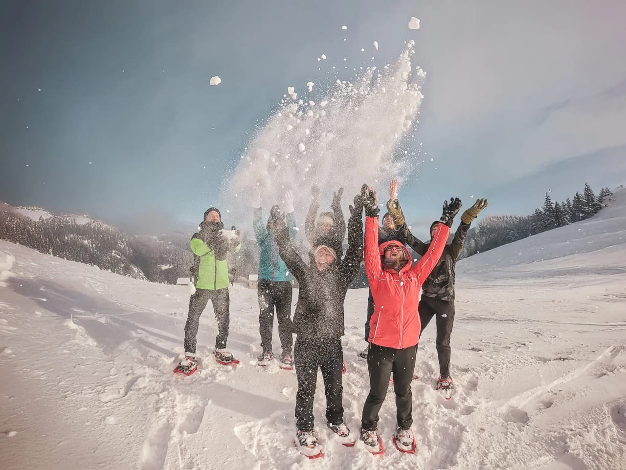 An enthusiastic group on snowshoes, throwing snow under a sunny sky in the Vosges.