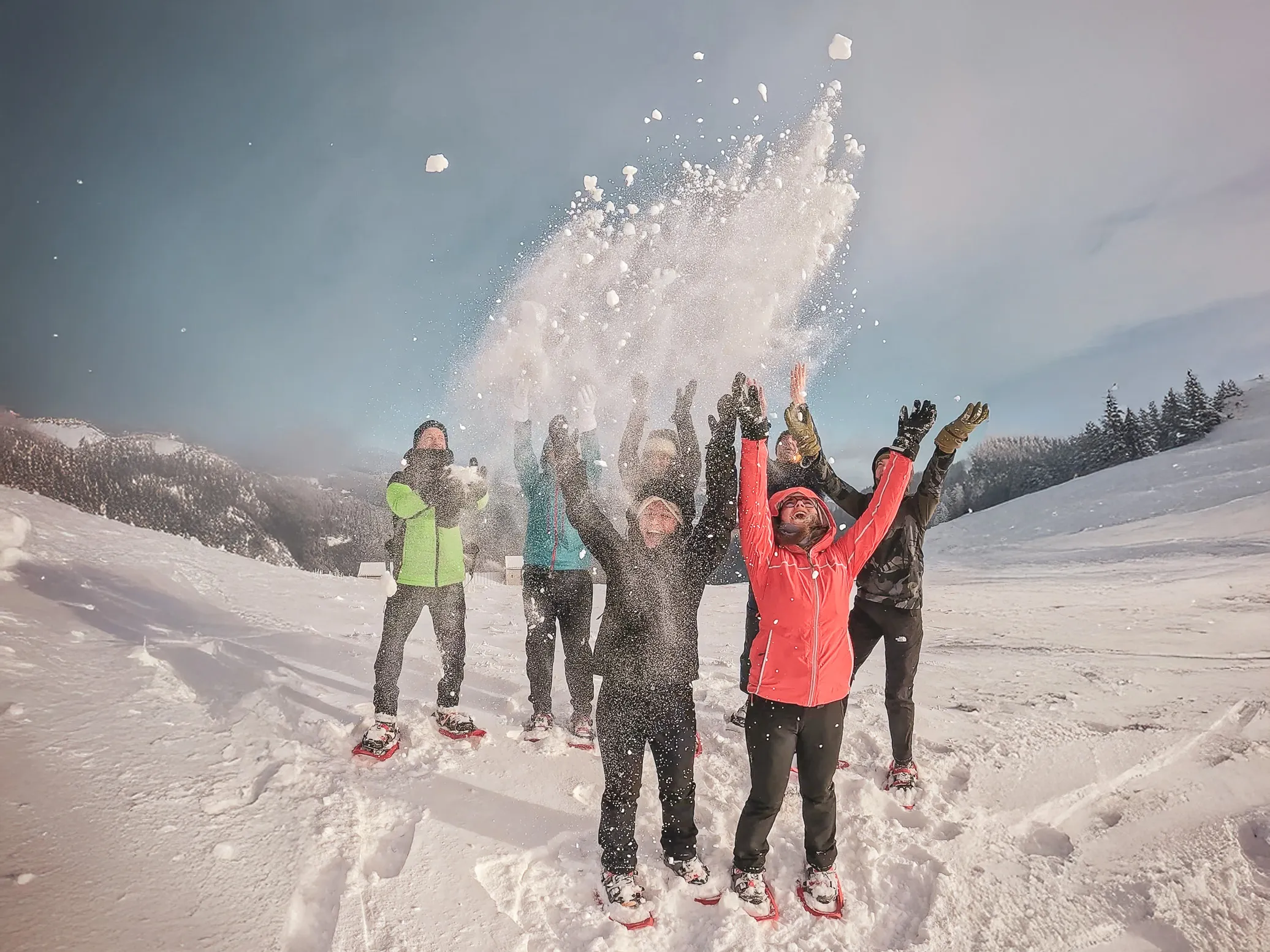 An enthusiastic group on snowshoes, throwing snow under a sunny sky in the Vosges.