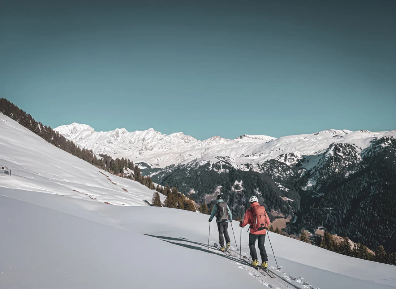 Two skiers make their way down snow-covered slopes, surrounded by majestic Alpine scenery.