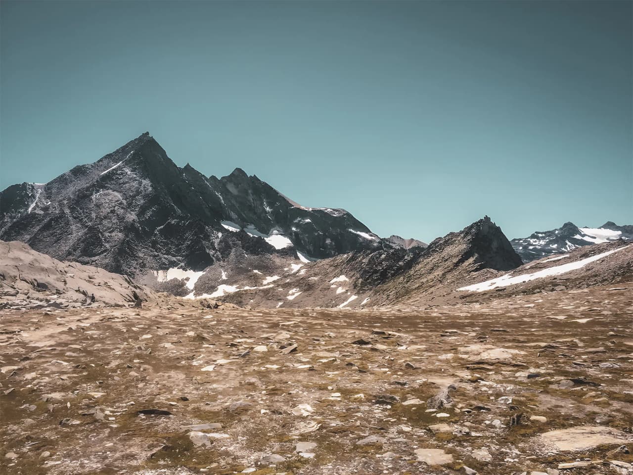 Majestic Alpine scenery with craggy peaks and vast meadows under a clear blue sky.